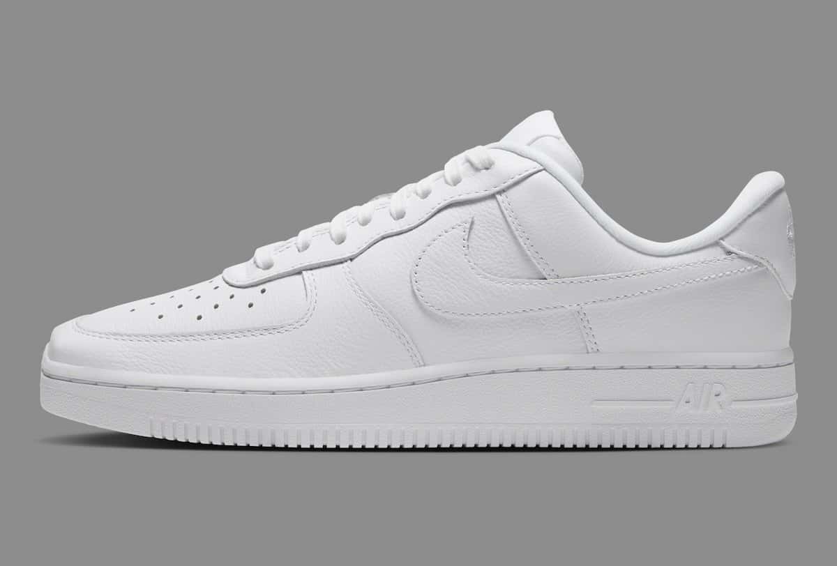 Nike Air Force 1 Low de punta cuadrada Triple White de perfil sobre fondo gris, toda de cuero blanco con la puntera más larga y plana
