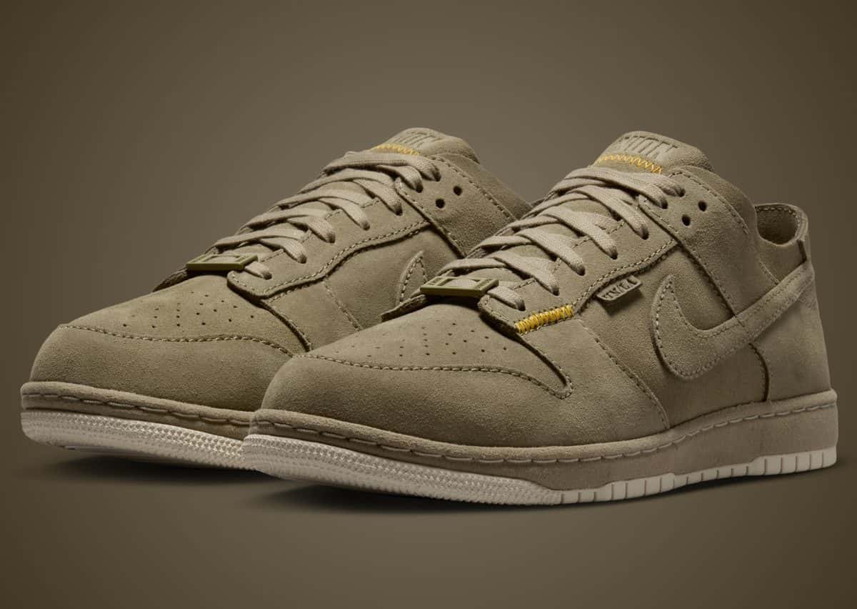 Par de Union x Nike Dunk Low Bamboo en gamuza color bambú, con costuras amarillas en la lengüeta y suela crema, sobre fondo marrón